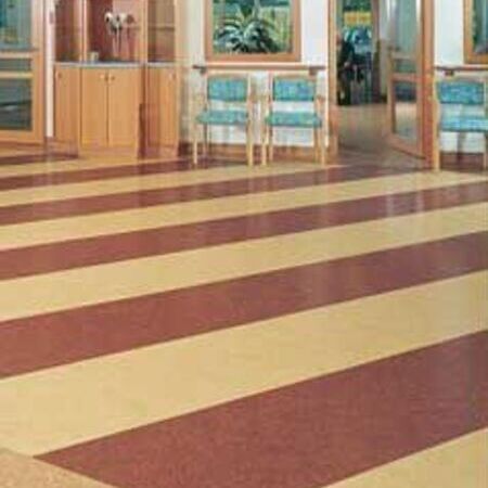 Ein Krankenhausflur mit gestreiftem Boden und Glastüren, die zu einem Wartebereich führen.